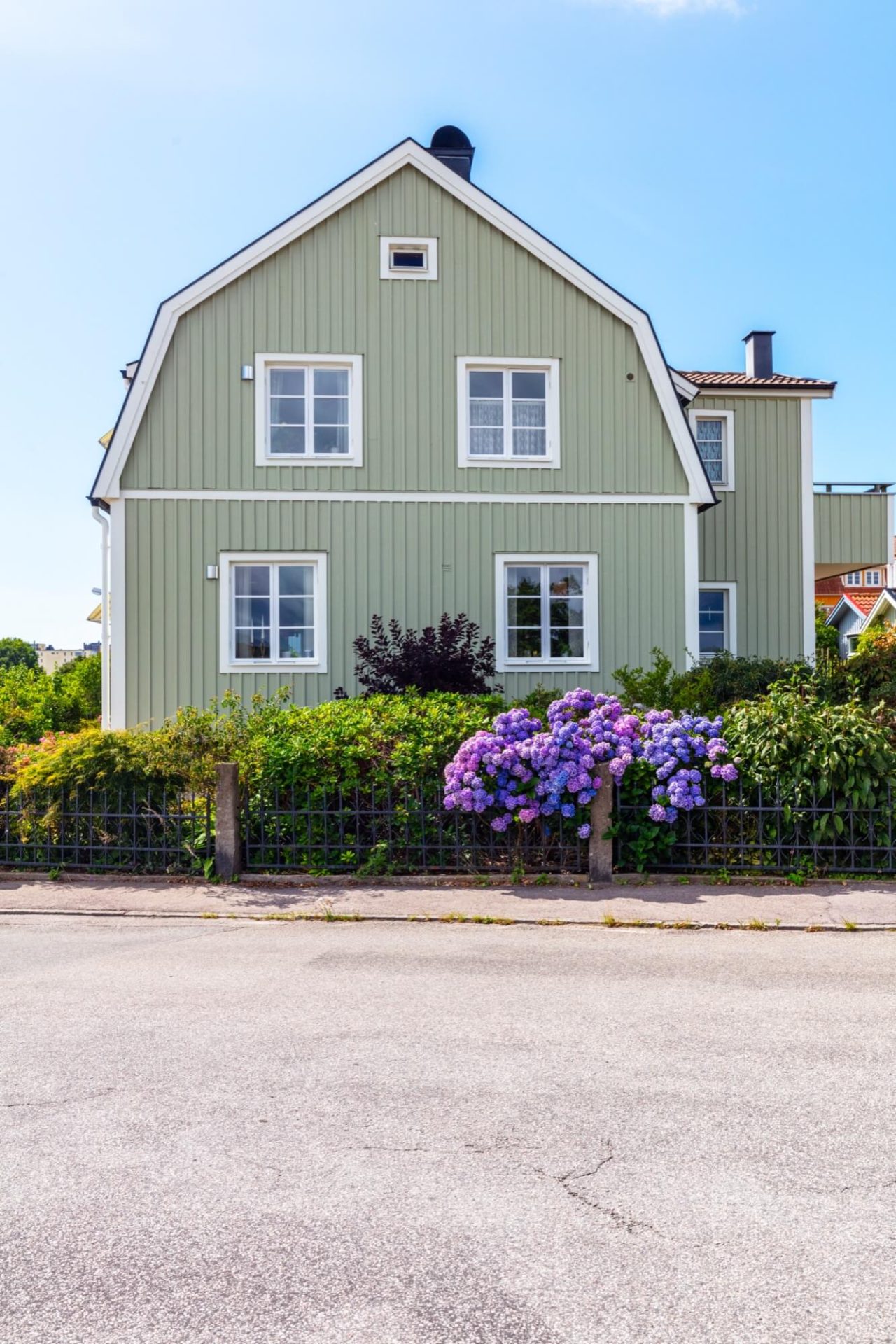En bostad vars träväggar är målade i grönt, kompletterat med vit fasaddekor och prydd med en trädgård av lila hortensior